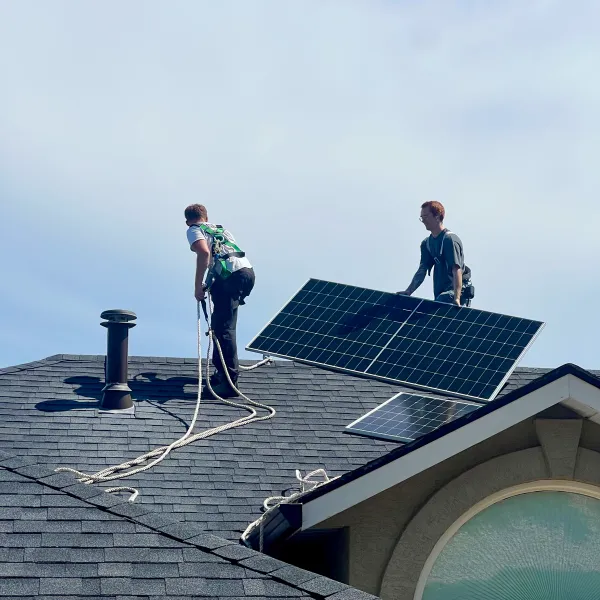 Two installers in harnesses carrying a solar panel across a roof